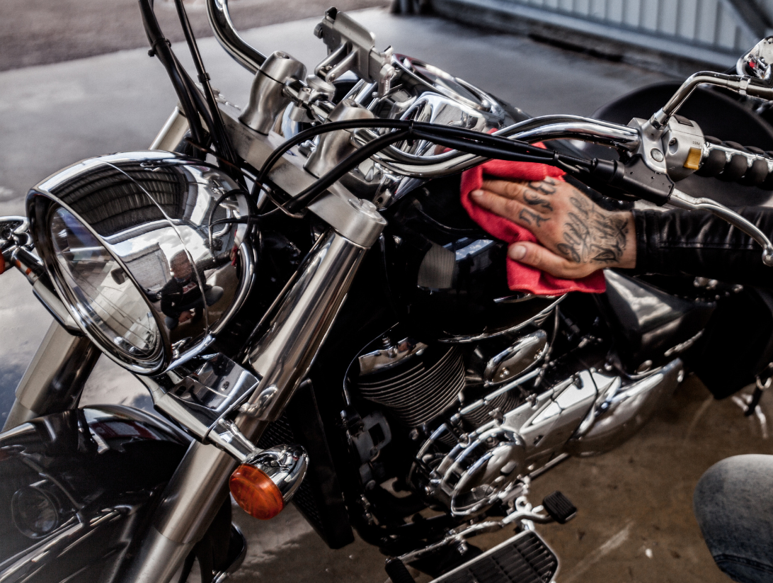 Mężczyzna dokładnie polerujący czarny bak motocykla typu cruiser czerwoną ściereczką z mikrofibry, profesjonalny detailing motocykla.