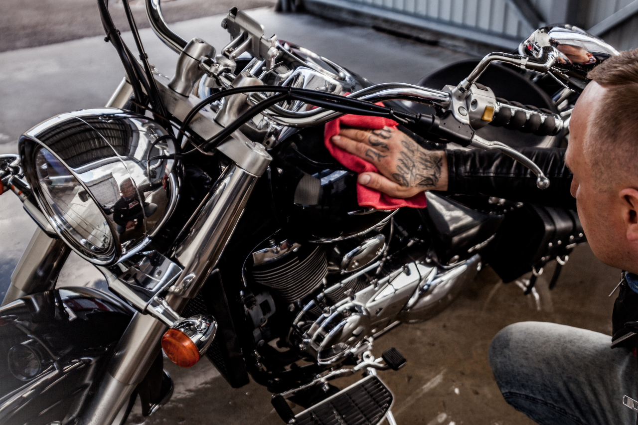 Mężczyzna dokładnie polerujący czarny bak motocykla typu cruiser czerwoną ściereczką z mikrofibry, profesjonalny detailing motocykla.